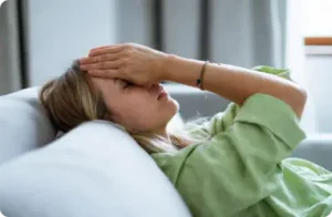 Woman lying down with her hand over her face due to a migraine.